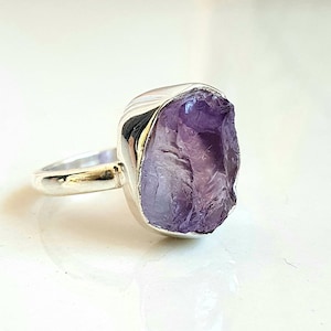 May include: A silver ring with a large, raw amethyst gemstone. The amethyst is a deep purple color and has a natural, rough texture.
