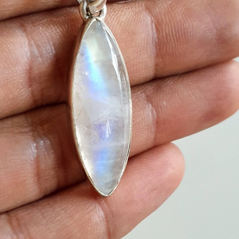 May include: A silver pendant featuring a large, oval-shaped moonstone with a rainbow sheen.