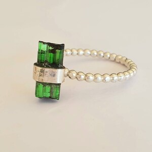 May include: A silver ring with a green tourmaline gemstone. The ring is made of small silver beads.