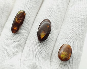 May include: Three oval-shaped agate cabochons with brown, orange, and green patterns. The cabochons are on a white fabric background.