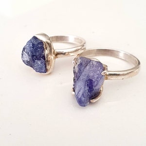 May include: Two silver rings with raw, blue-purple gemstone settings. The rings are stacked on top of each other.