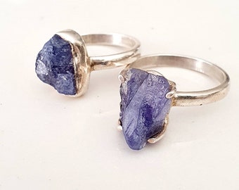 May include: Two silver rings with raw, blue-purple gemstone settings. The rings are stacked on top of each other.