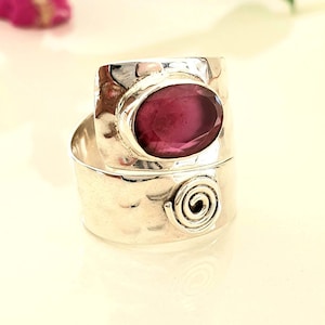 Może przedstawiać: Srebrny pierścionek z młotkowanym wykończeniem i spiralnym wzorem. Pierścionek zdobi duży, owalny, fioletowy kamień szlachetny.