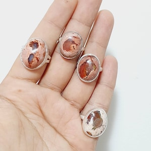 May include: Four silver rings with oval-shaped opal stones. The opals are a mix of white, brown, and orange.