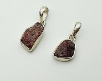 May include: Two silver pendants with raw, red-brown gemstones. The pendants are on a white background.
