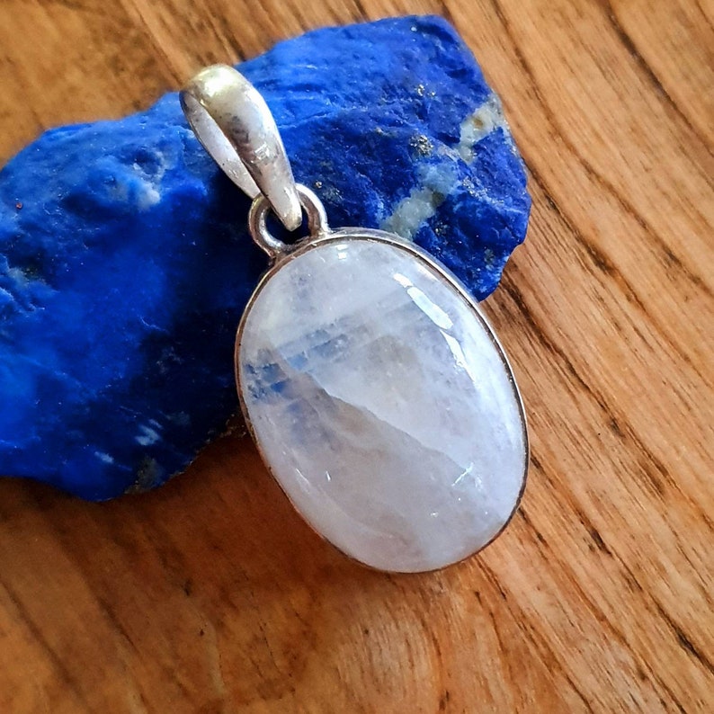 May include: A silver pendant with a white moonstone oval cabochon. The pendant is on a blue background.
