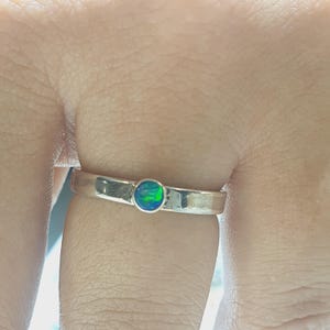 Puede incluir: Un anillo de plata con una piedra de ópalo verde engastada en el centro.