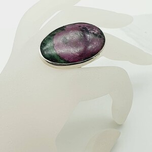 May include: A silver ring featuring a large oval green and pink gemstone.