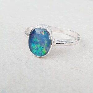May include: A silver ring with an oval-shaped opal gemstone. The opal has a blue, green, and iridescent color.