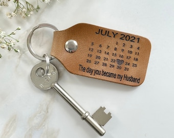 May include: A brown leather keychain with a silver key and a calendar charm. The calendar charm has the month of July 2021 and the text "The day you became my Husband".
