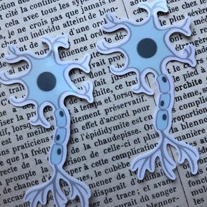 Pode incluir: Dois recortes de papel em forma de neurónio azul claro com centros cinza escuro e ramificações, colocados sobre um fundo de jornal vintage. Os recortes são detalhados com detalhes em azul claro e cinza.