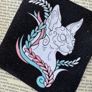 May include: A square black fabric patch featuring a white line-art illustration of a cat head in profile. The cat is surrounded by stylised leafy branches coloured in alternating light blue and soft pink, creating a decorative botanical frame.