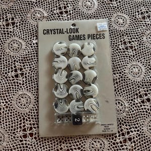 Op de afbeelding: Een pakket kristal-look spelstukken. Het pakket bevat 16 wit en zwart gewervelde spelstukken en twee dobbelstenen. De tekst op de verpakking luidt "CRYSTAL-LOOK GAMES PIECES".