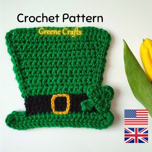 Pode incluir: Padrão de crochê para um chapéu de duende verde com uma faixa preta e uma fivela dourada. O chapéu tem um trevo verde no lado. O padrão está disponível em inglês americano e britânico.