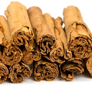 Op de afbeelding: Een verzameling kaneelstokjes, die hun gerolde vorm en warme bruine kleur laten zien. De afbeelding benadrukt de textuur en het natuurlijke uiterlijk van de specerij, perfect voor culinair gebruik of decoratieve doeleinden.