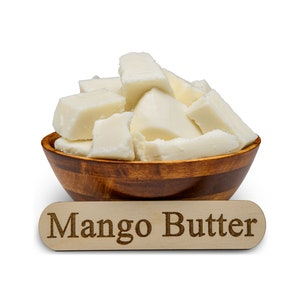 May include: A wooden bowl filled with chunks of white mango butter. The bowl is sitting on a white surface with a wooden sign that reads "Mango Butter".