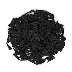 Op de afbeelding: Een grote hoop zwarte wierookkegels, elk met een conische vorm en een getextureerd oppervlak. De kegels zijn dicht op elkaar gepakt tegen een witte achtergrond, wat een opvallend visueel contrast cre&euml;ert.