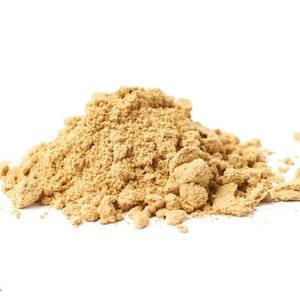 Puede incluir: Un mont&oacute;n de polvo marr&oacute;n claro sobre un fondo blanco. El polvo, de textura fina y granulada, parece ser una especia o ingrediente culinario. La imagen est&aacute; bien iluminada, destacando la textura y el color del polvo.