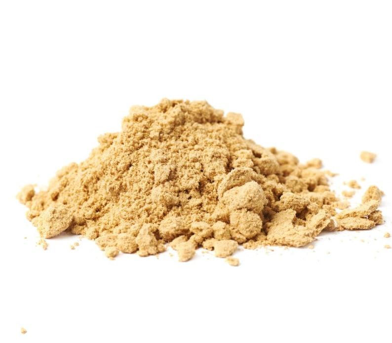 Puede incluir: Un mont&oacute;n de polvo marr&oacute;n claro sobre un fondo blanco. El polvo, de textura fina y granulada, parece ser una especia o ingrediente culinario. La imagen est&aacute; bien iluminada, destacando la textura y el color del polvo.