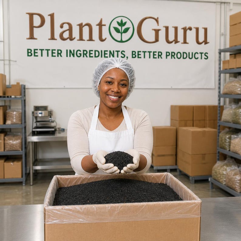 May include: A person wearing a white hairnet, white apron, and white gloves holds a handful of small black granules over a large cardboard box filled with the same black material. A banner behind reads Plant Guru BETTER INGREDIENTS, BETTER PRODUCTS.