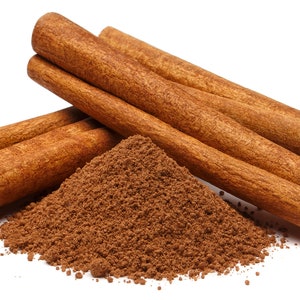 May include: Close-up of cinnamon sticks and ground cinnamon. The cinnamon sticks are a warm brown color, with a textured surface and curled ends. A pile of ground cinnamon is next to the sticks. The image is on a white background.