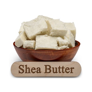 May include: A wooden bowl filled with chunks of white shea butter. A wooden sign below the bowl reads "Shea Butter".