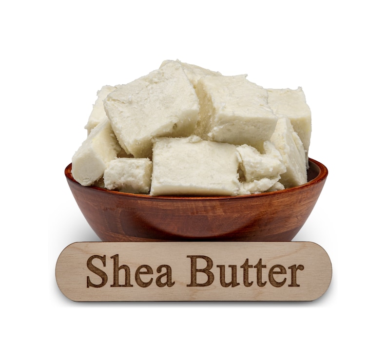 May include: A wooden bowl filled with chunks of white shea butter. A wooden sign below the bowl reads "Shea Butter".
