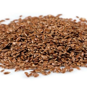 May include: A close-up view of a pile of brown flax seeds, also known as linseed, on a white background.