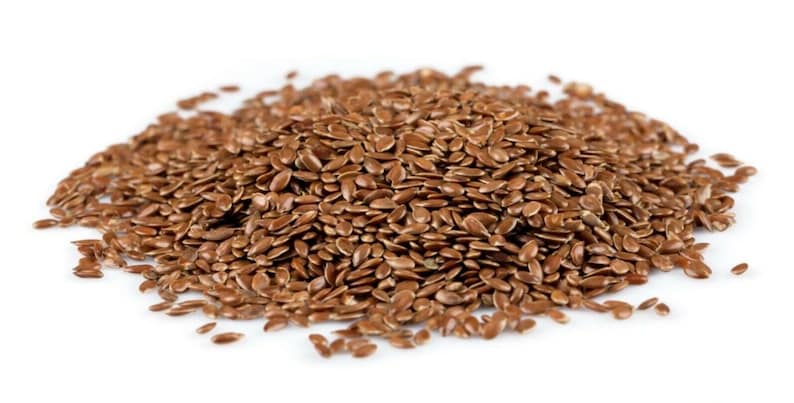May include: A close-up view of a pile of brown flax seeds, also known as linseed, on a white background.
