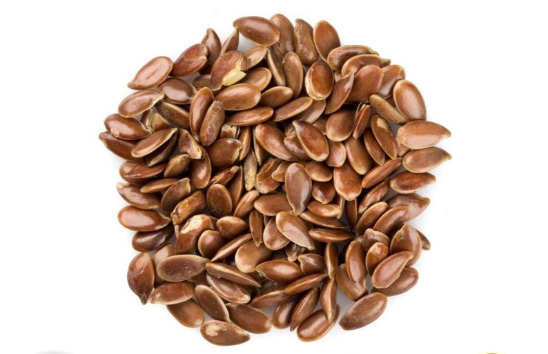 May include: A close-up view of a pile of brown flax seeds, also known as linseed, on a white background.