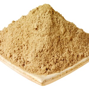 Puede incluir: Un polvo beige, posiblemente una especia o hierba, se amontona en un plato cuadrado de cer&aacute;mica de color claro. El polvo tiene una textura fina y granulada y un tono marr&oacute;n claro. El plato tiene un borde ligeramente elevado.