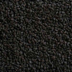 May include: Close-up shot of a pile of black seeds. The seeds are small, oval-shaped, and densely packed together, filling the frame. The color is a deep, uniform black, with a slightly glossy sheen.