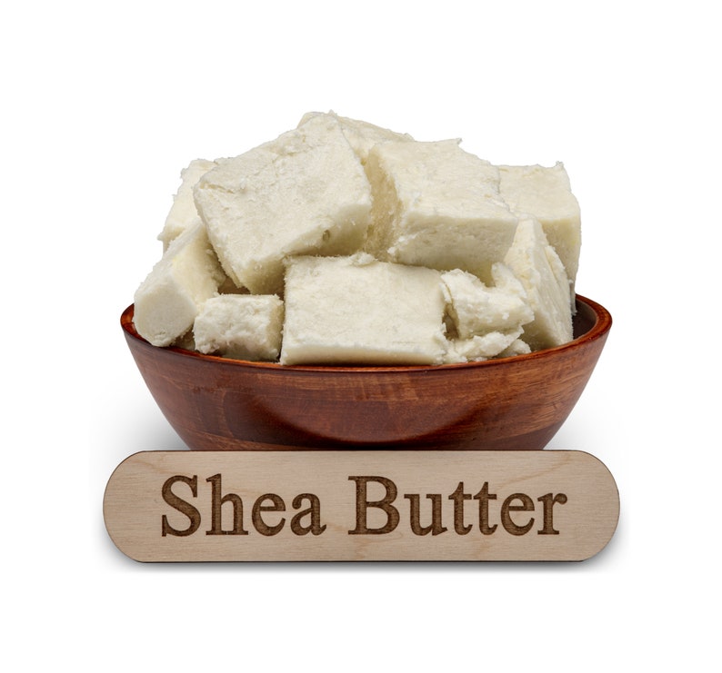 Może przedstawiać: Drewniana miska wypełniona kawałkami białego masła shea. Drewniany napis pod miską głosi "Shea Butter".