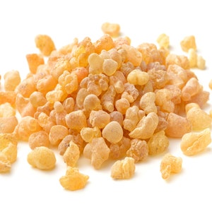 May include: A close-up of a pile of pale yellow resin pieces, also known as frankincense, on a white background.