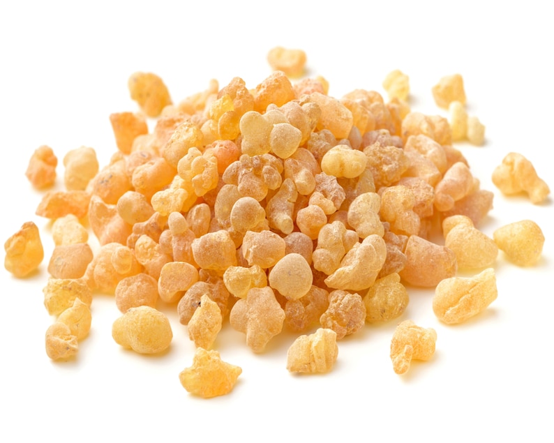 May include: A close-up of a pile of pale yellow resin pieces, also known as frankincense, on a white background.