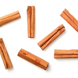 Op de afbeelding: Luchtfoto van verschillende kaneelstokjes verspreid op een witte achtergrond. De stokjes hebben een warme bruine kleur, met een textuur. De afbeelding is goed belicht, waardoor de natuurlijke kleur en textuur van de specerij worden benadrukt.