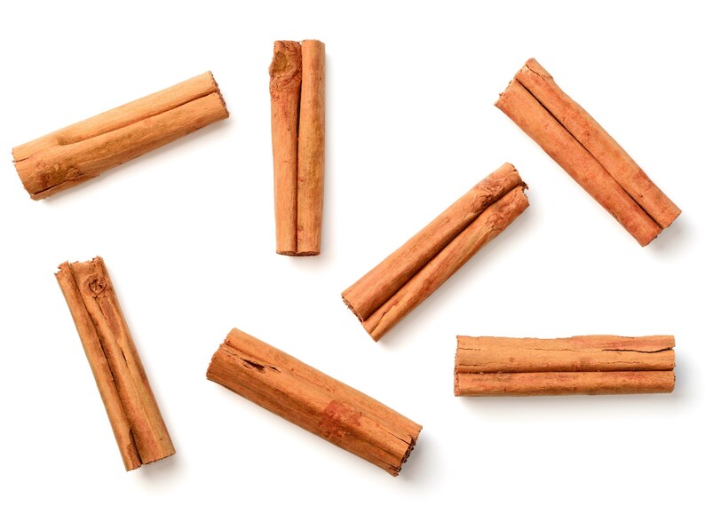 Op de afbeelding: Luchtfoto van verschillende kaneelstokjes verspreid op een witte achtergrond. De stokjes hebben een warme bruine kleur, met een textuur. De afbeelding is goed belicht, waardoor de natuurlijke kleur en textuur van de specerij worden benadrukt.