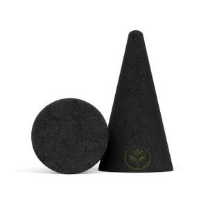 May include: A black incense cone and a round incense holder. The cone is textured and has a green leaf logo. The incense holder is a flat, circular disc. Both items are set against a white background.