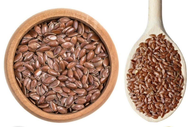 May include: A wooden bowl and spoon filled with brown flax seeds.
