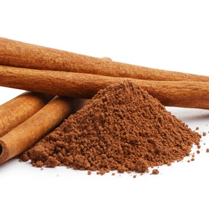 May include: Close-up of cinnamon sticks and ground cinnamon. Three whole cinnamon sticks are arranged with a pile of ground cinnamon. The cinnamon sticks are a warm brown color, and the ground cinnamon is a darker brown.