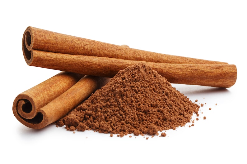 May include: Close-up of cinnamon sticks and ground cinnamon. Three whole cinnamon sticks are arranged with a pile of ground cinnamon. The cinnamon sticks are a warm brown color, and the ground cinnamon is a darker brown.