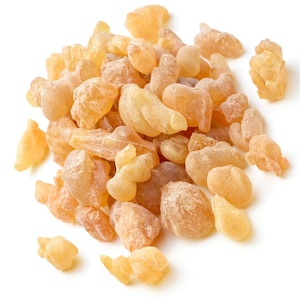 May include: A pile of light brown resin pieces, also known as frankincense, on a white background.