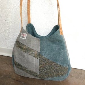 May include: A patchwork tote bag in teal and grey, with a herringbone pattern and cork handles. A small label is sewn on the side of the bag. The bag is designed for carrying items.