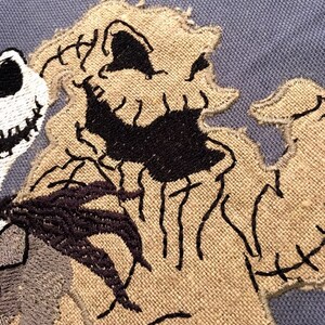 May include: Close-up of a brown and black embroidered patch featuring the character Jack Skellington from the movie The Nightmare Before Christmas. The patch is stitched with a detailed design of Jack's face and body.