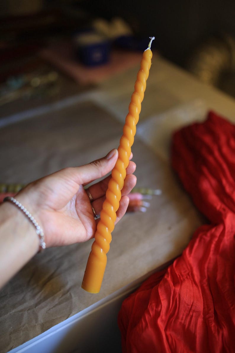 K&ouml;nnte beinhalten: Eine lange, schlanke, goldgelbe Stabkerze mit einem durchgehenden, gedrehten Spiralmuster &uuml;ber die gesamte L&auml;nge. Die Kerze hat eine glatte, wachsartige Textur und einen einzelnen wei&szlig;en Baumwolldocht am oberen Ende.