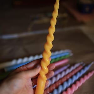 K&ouml;nnte beinhalten: Eine lange, gelbe Stabkerze mit gedrehtem Spiraldesign. Die Kerze hat einen glatten, zylindrischen Fu&szlig;, der in einen sich verj&uuml;ngenden, spiralf&ouml;rmigen oberen Teil &uuml;bergeht, mit einem kleinen wei&szlig;en Docht an der Spitze, in vertikaler Haltung.
