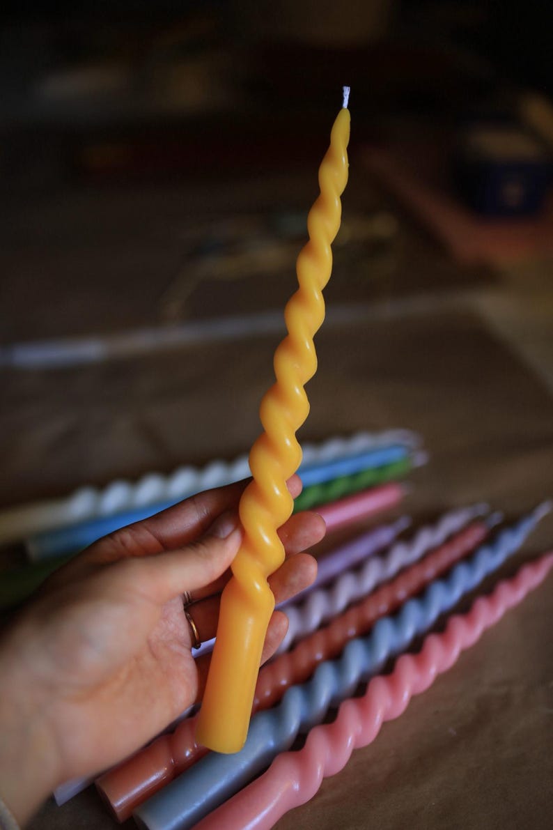K&ouml;nnte beinhalten: Eine lange, gelbe Stabkerze mit gedrehtem Spiraldesign. Die Kerze hat einen glatten, zylindrischen Fu&szlig;, der in einen sich verj&uuml;ngenden, spiralf&ouml;rmigen oberen Teil &uuml;bergeht, mit einem kleinen wei&szlig;en Docht an der Spitze, in vertikaler Haltung.