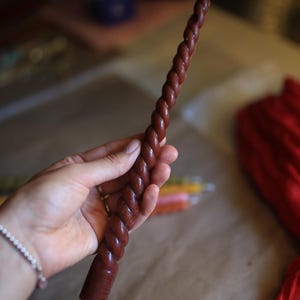 K&ouml;nnte beinhalten: Eine lange, schlanke, dunkelbraune Stabkerze mit einer ausgepr&auml;gten, gedrehten, seilartigen Textur &uuml;ber die gesamte L&auml;nge. Die Kerze hat einen flachen, zylindrischen Fu&szlig; und einen einzelnen wei&szlig;en Baumwolldocht an der Spitze in einheitlicher Farbe.