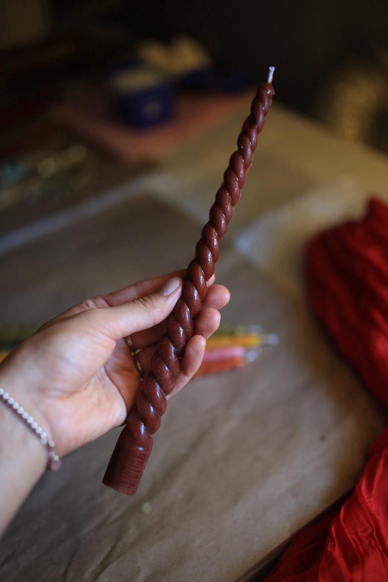 K&ouml;nnte beinhalten: Eine lange, schlanke, dunkelbraune Stabkerze mit einer ausgepr&auml;gten, gedrehten, seilartigen Textur &uuml;ber die gesamte L&auml;nge. Die Kerze hat einen flachen, zylindrischen Fu&szlig; und einen einzelnen wei&szlig;en Baumwolldocht an der Spitze in einheitlicher Farbe.