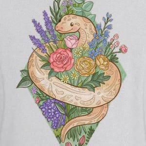 May include: A light grey hooded sweatshirt featuring a back graphic of a tan snake coiled around a colourful bouquet of flowers including pink roses, yellow blossoms, and purple lavender, all set against a diamond-shaped green background.